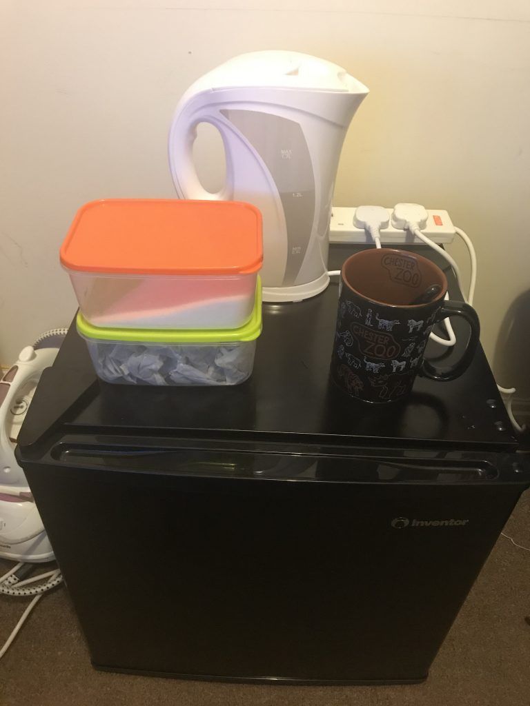Black fridge with white kettle and large mug of tea